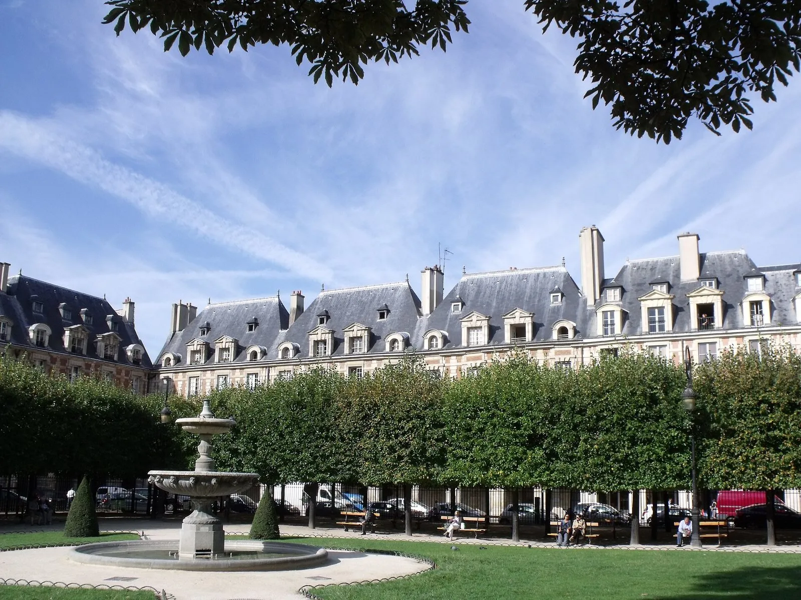 Les pavillons de brique rouge et de pierre de la place des Vosges, vus par-dessus la pelouse et la fontaine